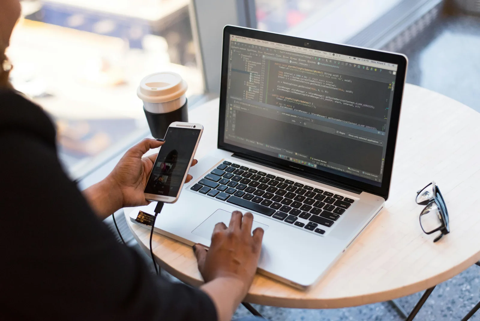 Personne utilisant un téléphone près d’un ordinateur affichant du code source