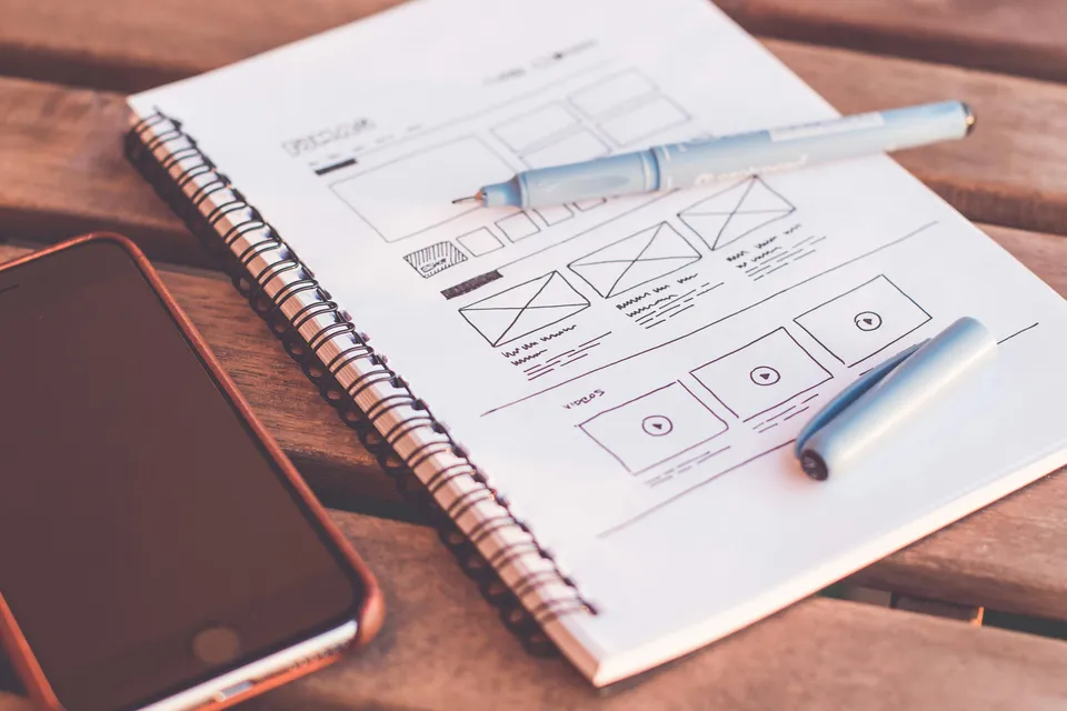 Notebook with hand-drawn interface sketches beside a phone